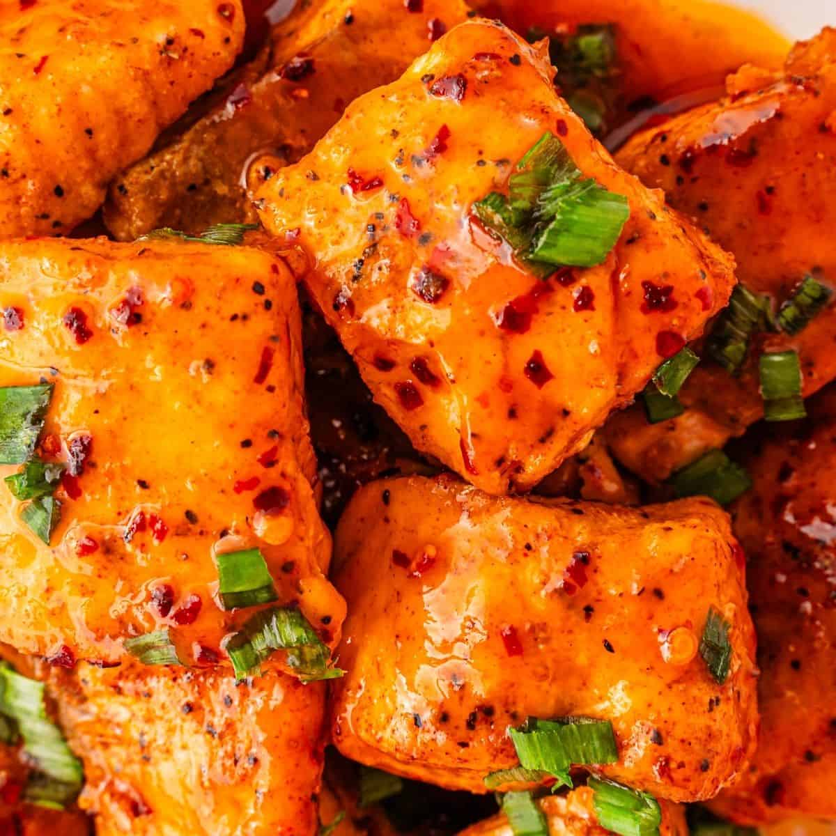 Hot honey-glazed salmon bites in a bowl, ready to serve with green onions on top