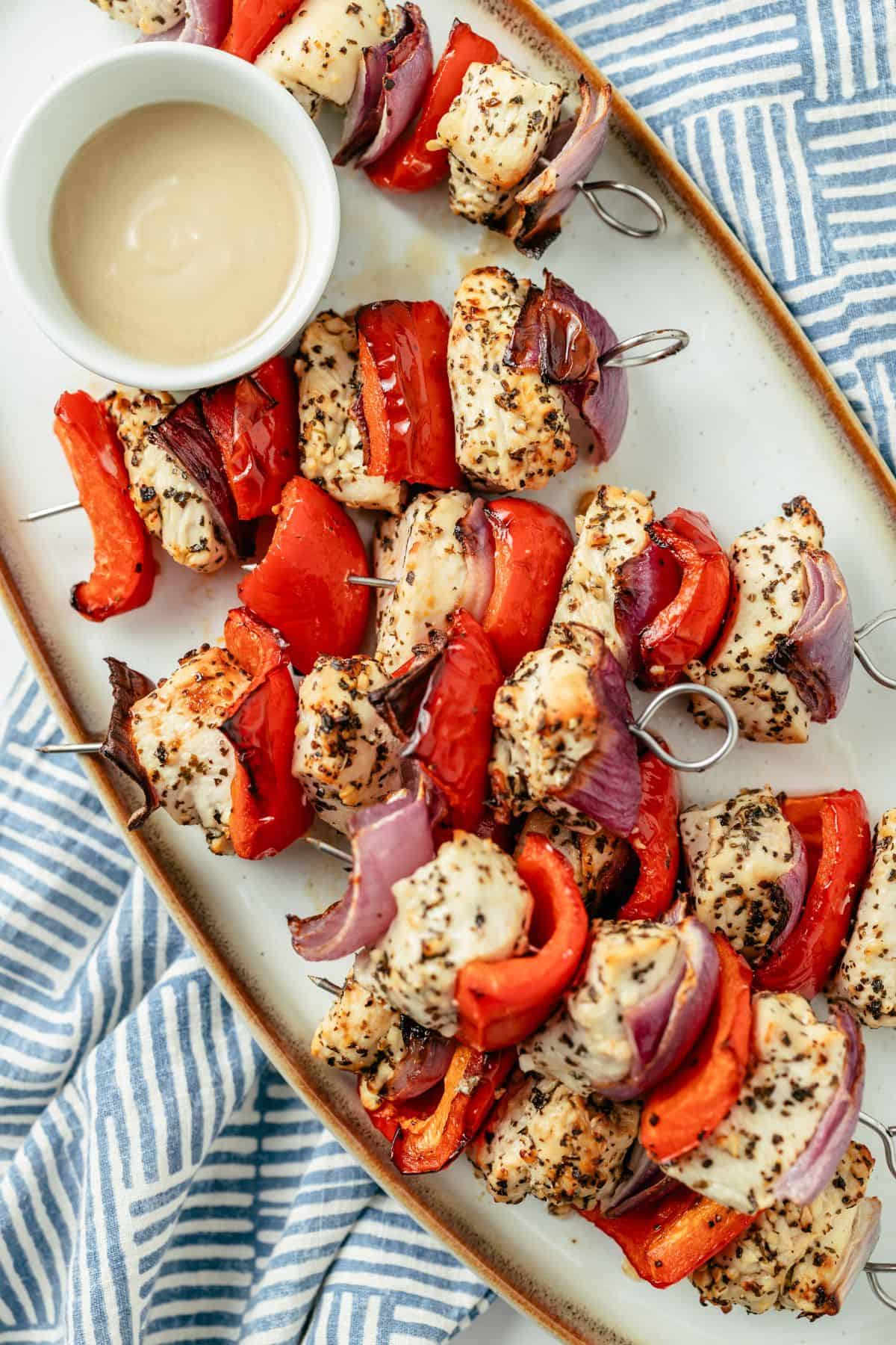 marinated chicken kabobs with a dipping sauce on a serving plate