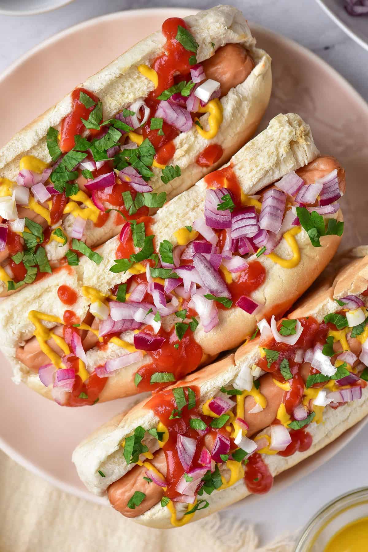 Crispy-edged air fryer hot dogs in buns topped with red onion and sauce