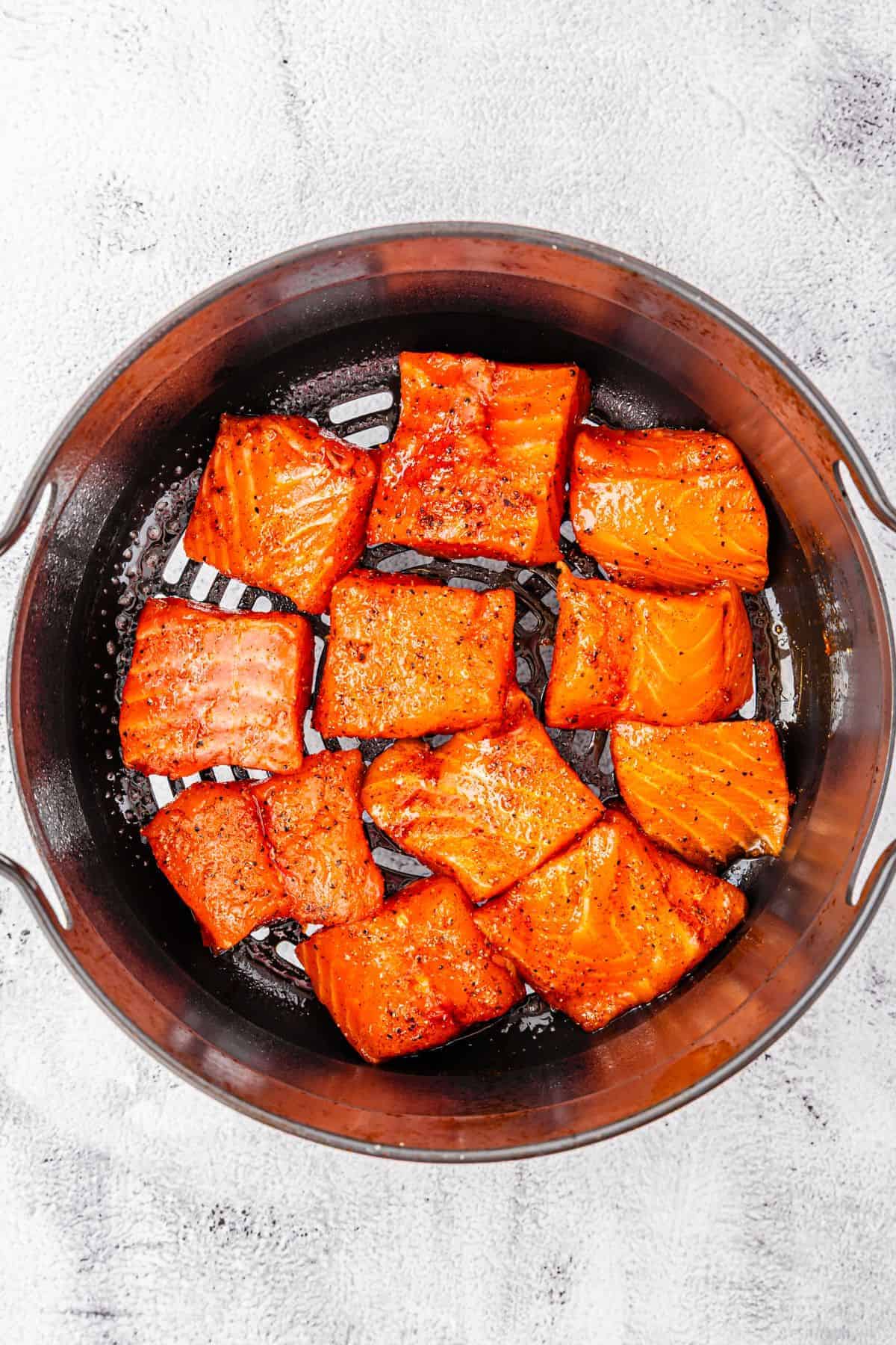 seasoned salmon bites in a single layer in an air fryer basket