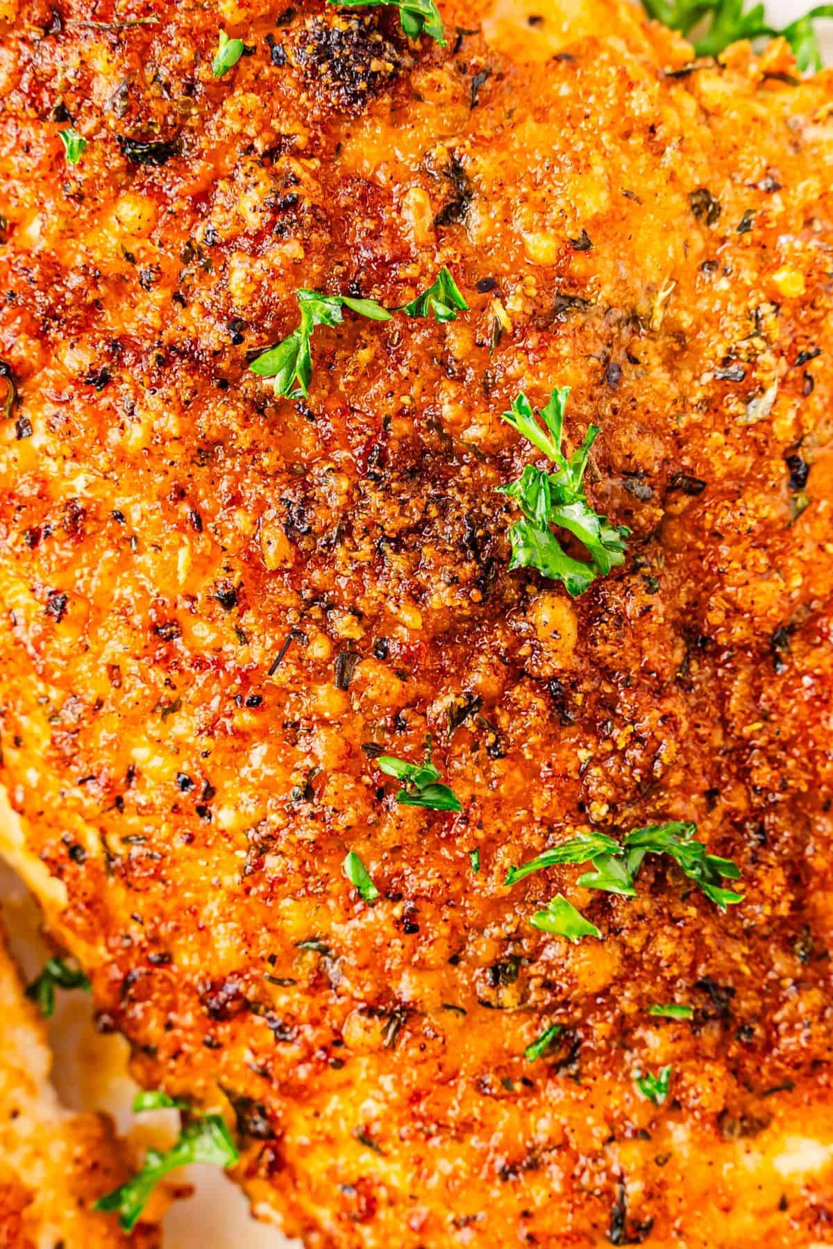 close-up of the parmesan crust on easy Parmesan crusted chicken breast with golden edges on white plate