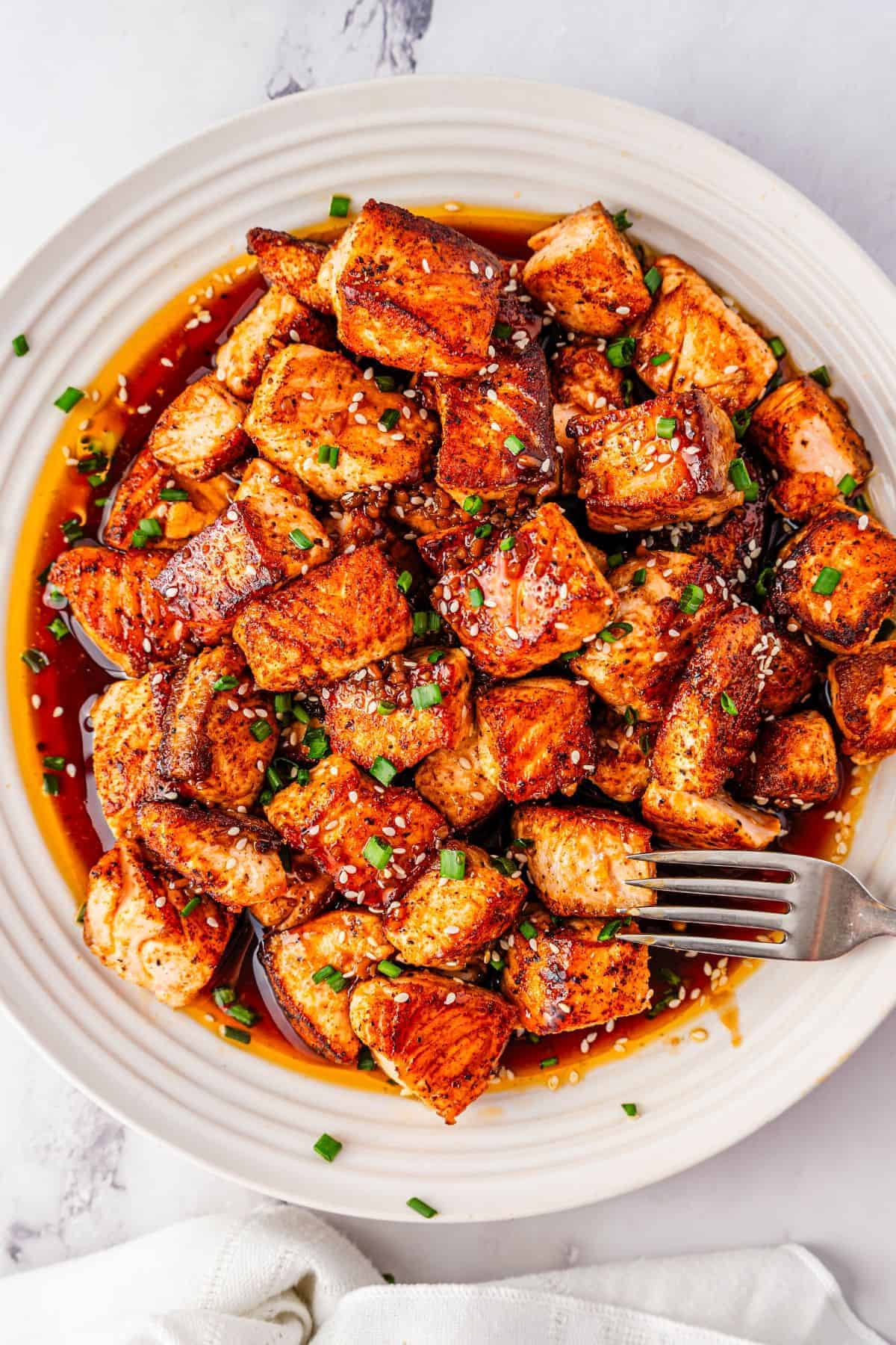 Flavorful teriyaki salmon bites on a plate with a fresh chive topping