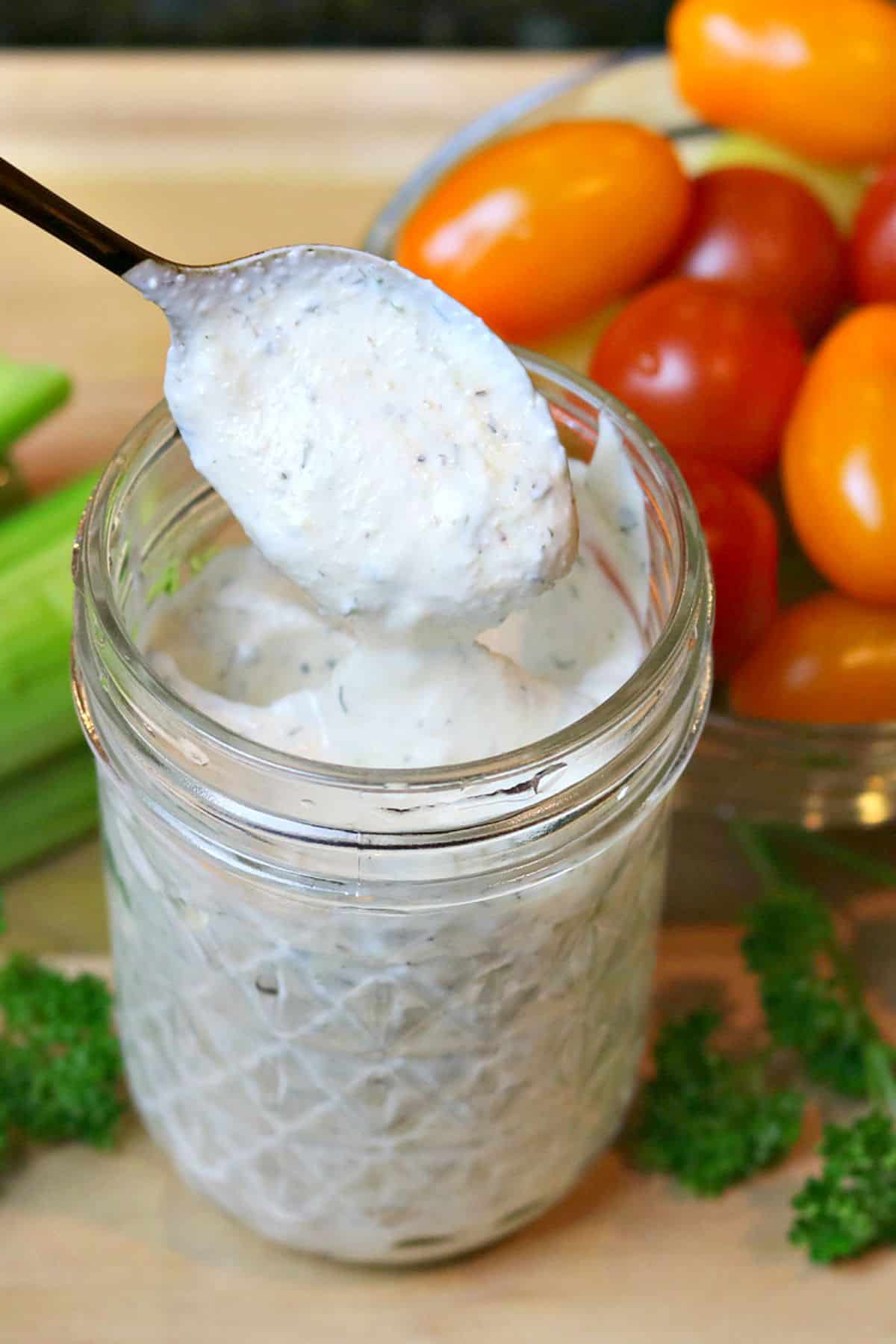 close-up of homemade ranch dressing in a glass jar being scooped out with a spoon