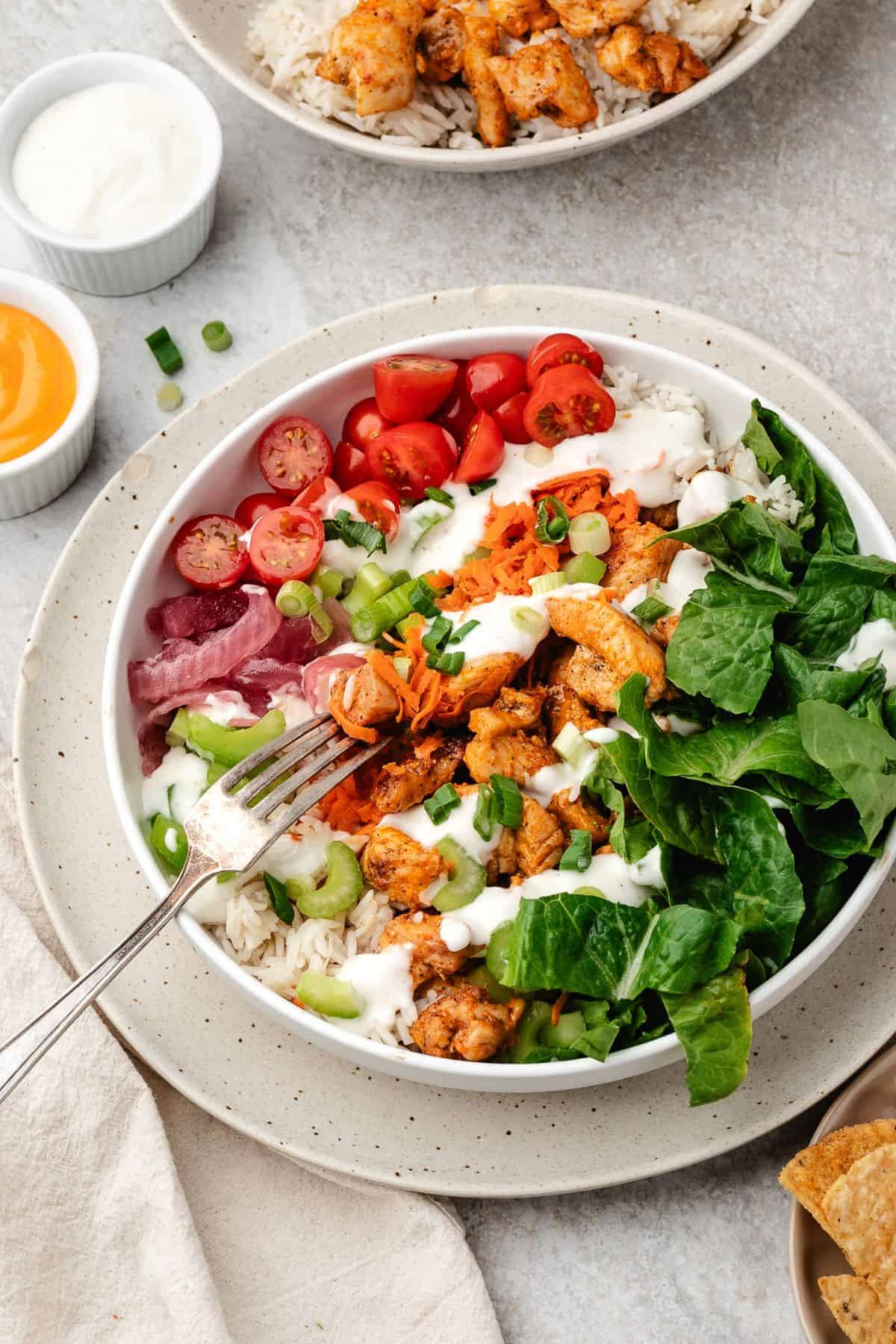 Healthy buffalo chicken rice bowl with celery, carrots, and optional cheese topping