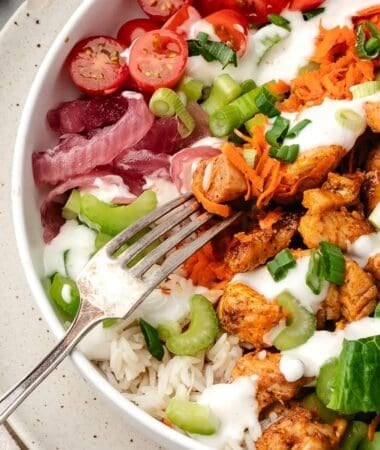 Homemade buffalo chicken bowl layered with rice, veggies, and melted cheese