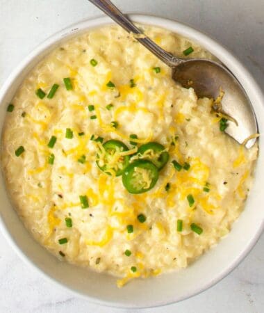 cheesy cauliflower grits recipe in a bowl topped with shredded cheddar cheese and chives