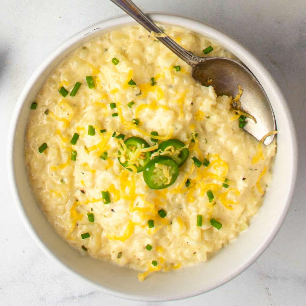 cheesy cauliflower grits recipe in a bowl topped with shredded cheddar cheese and chives
