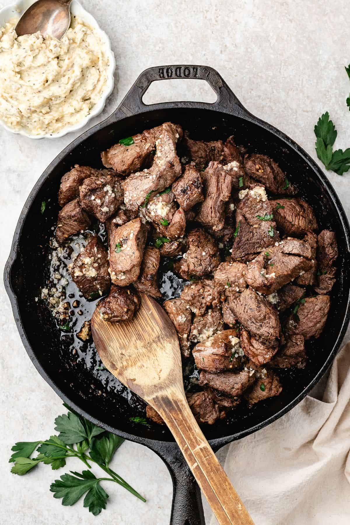 garlic butter steak bites recipe in a cast iron pan with a small bowl of garlic butter on the side