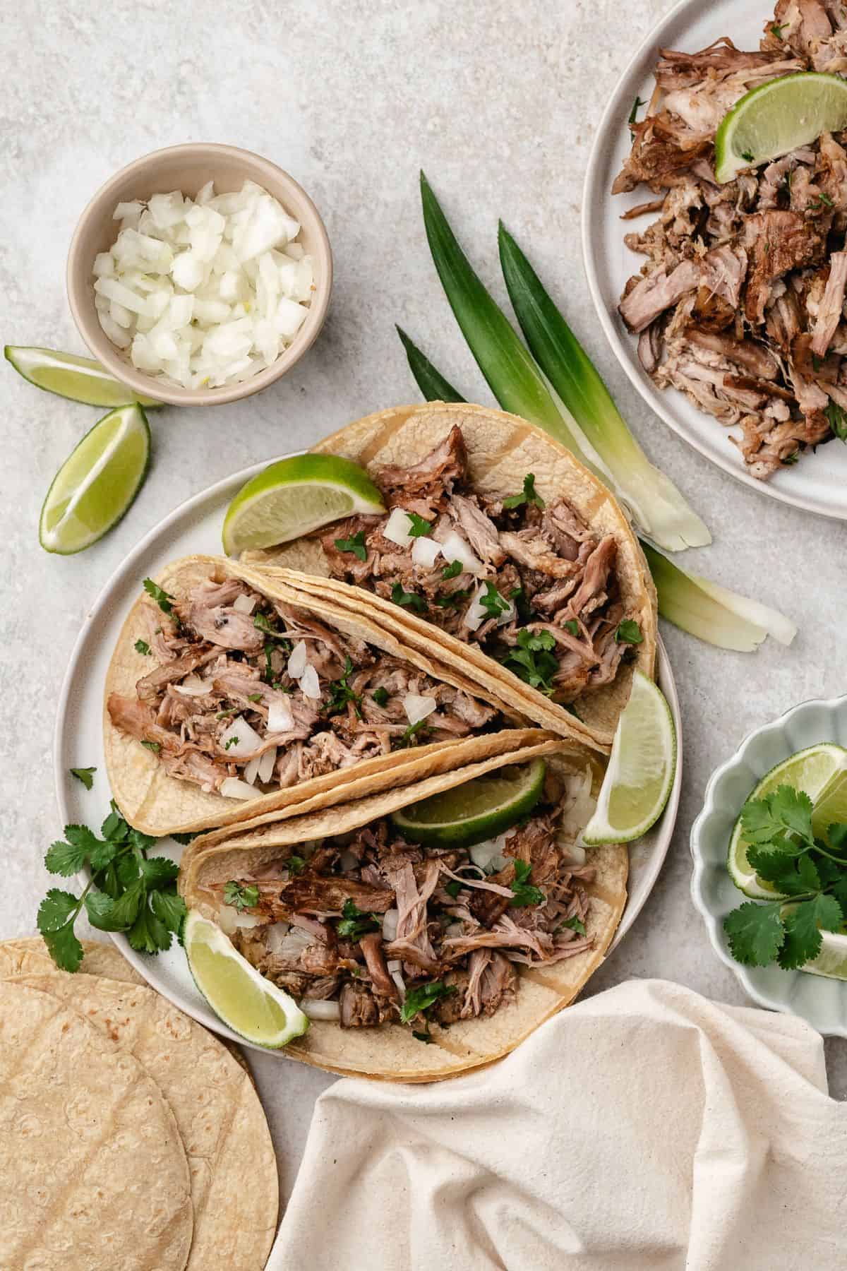 Tender shredded pork carnitas tacos with a crispy finish topped with cilantro, onions, and limes