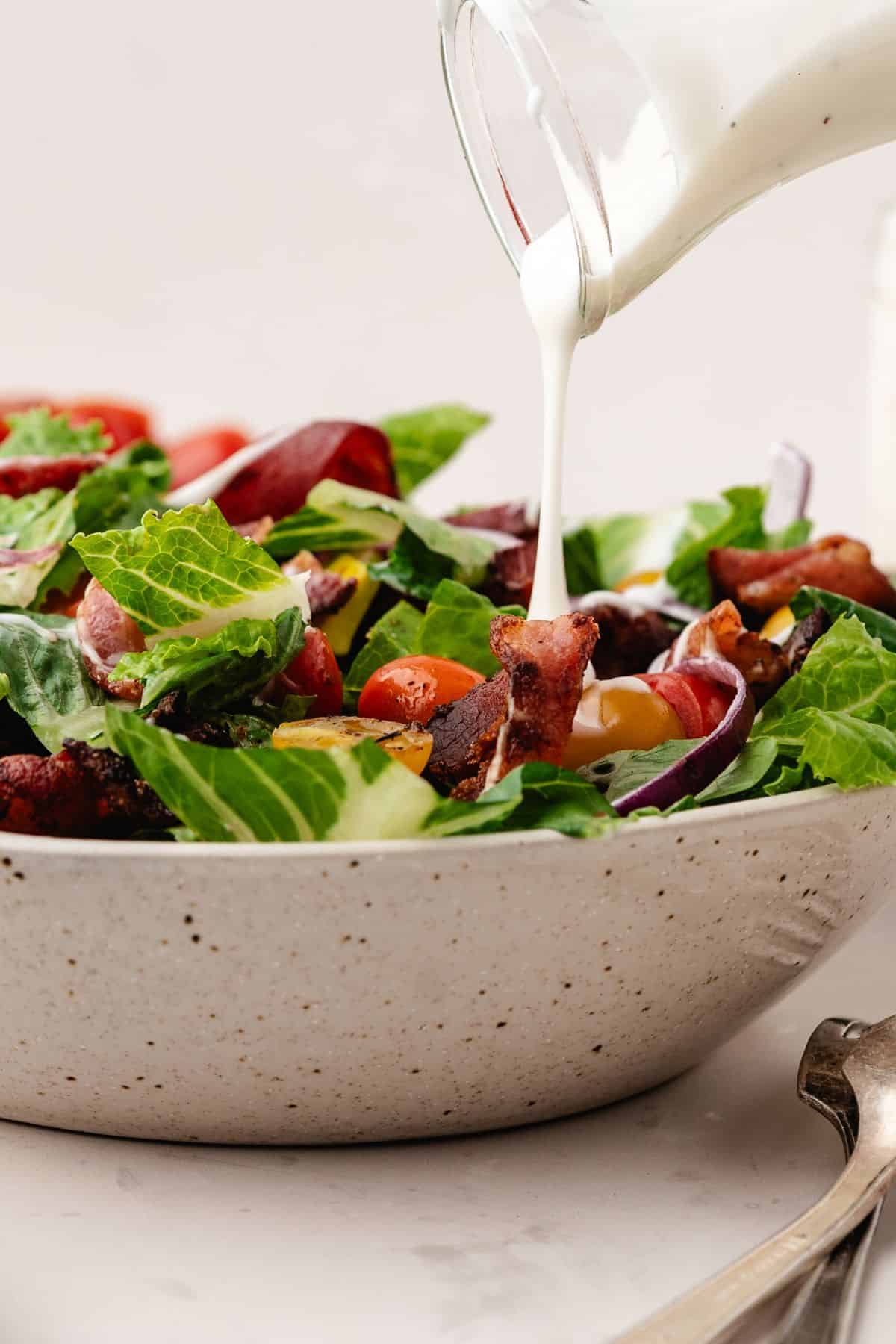 a blt salad in a bowl with ranch dressing being poured on top from a jar