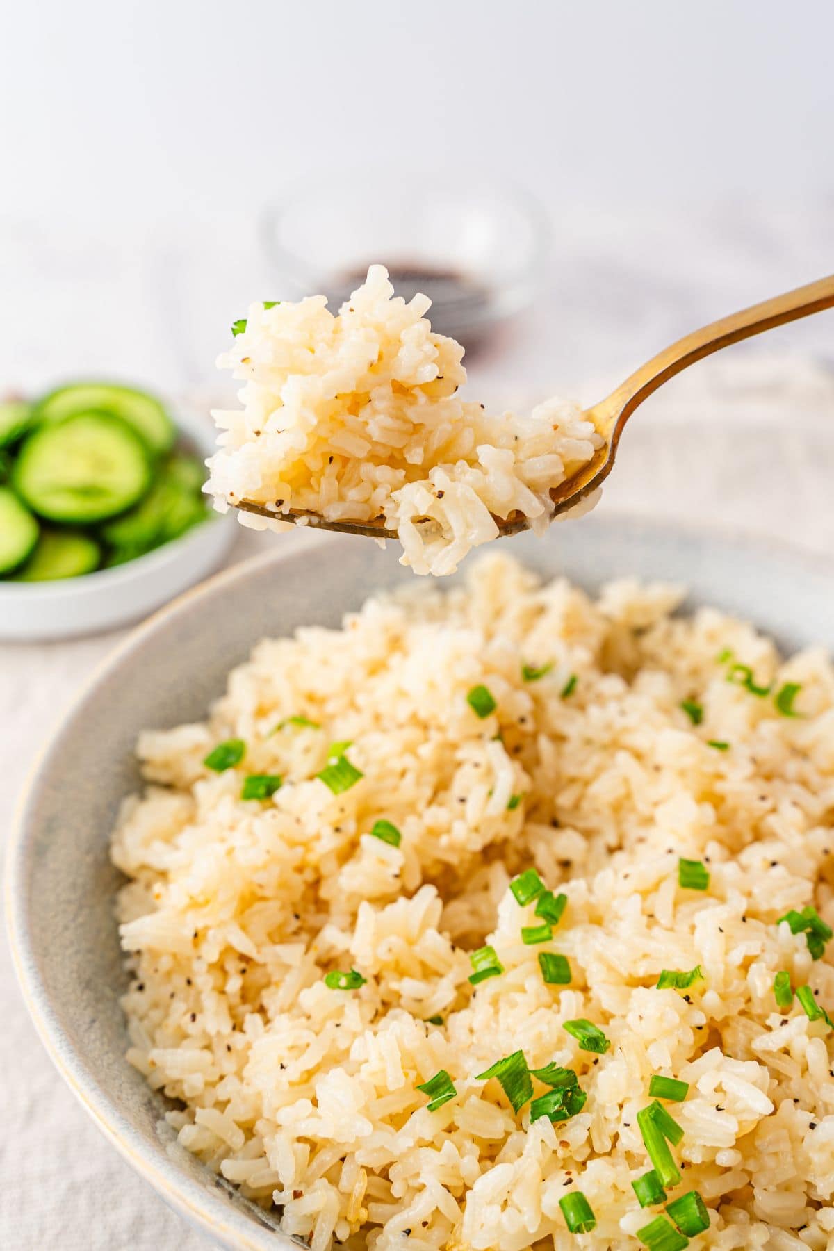 seasoned jasmine rice in a bowl with cucumber onion salad in the back