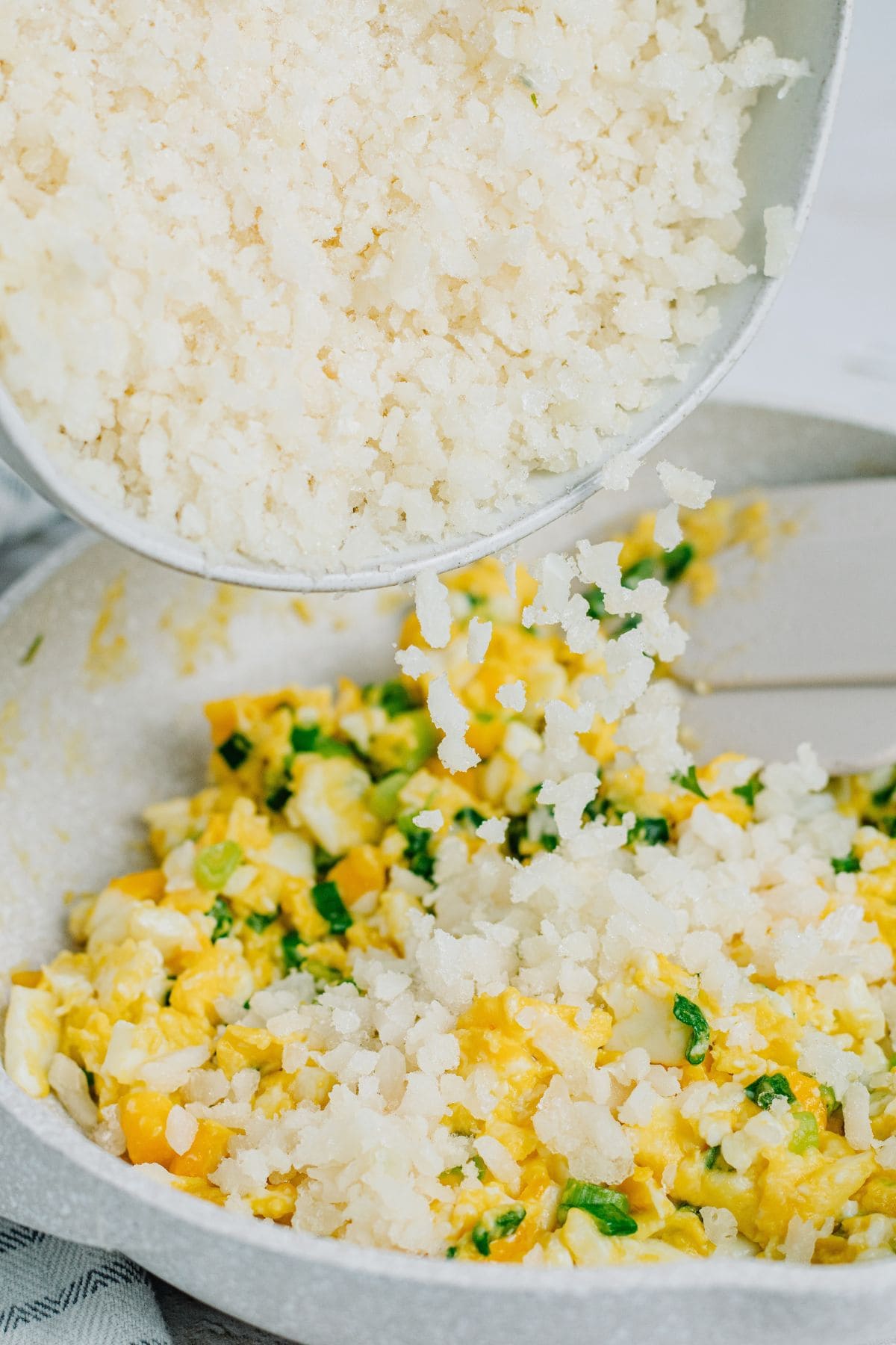 adding cauliflower rice to cooked green onions and scrambled eggs