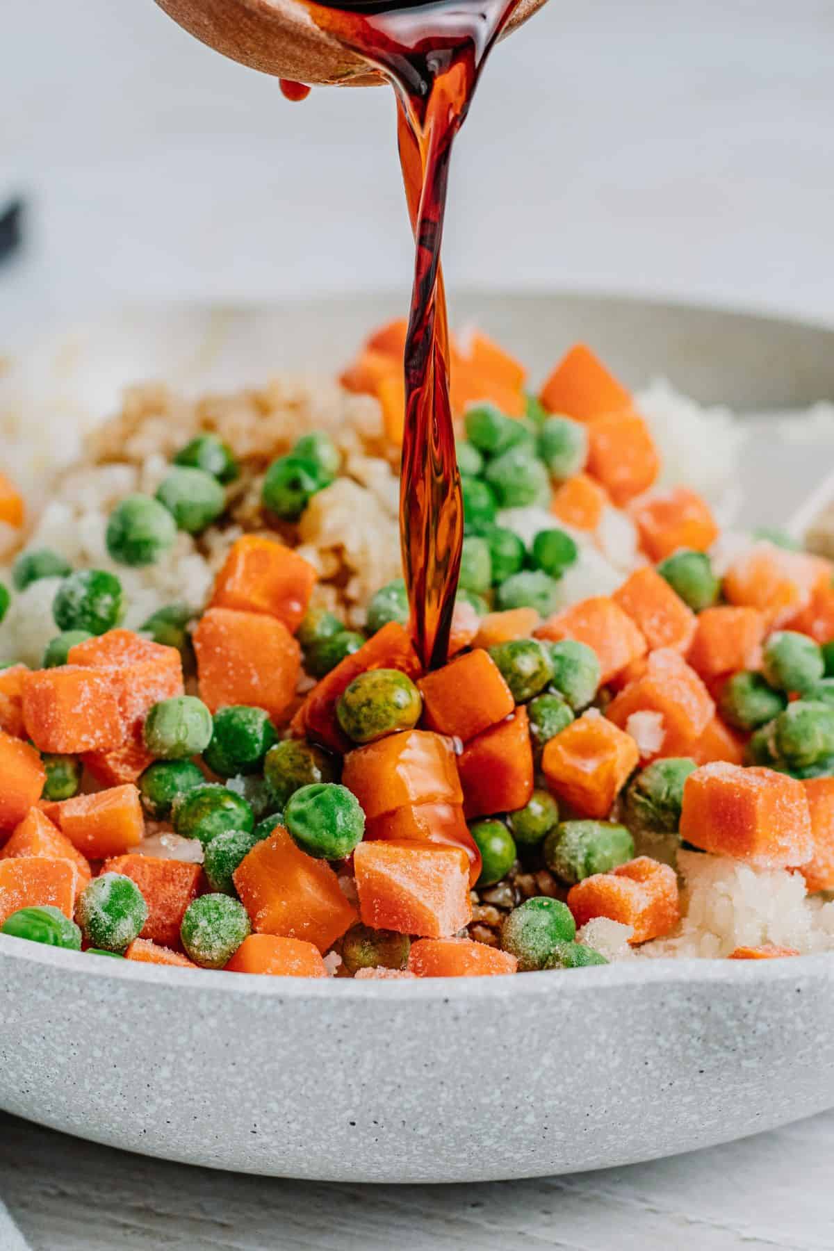 pouring coconut aminos, mixed vegetables, and fish sauce into keto fried rice to finish cooking it