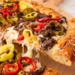 Philly steak pizza served hot with creamy cheese sauce and peppers