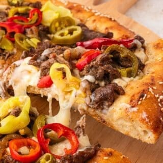 Philly steak pizza served hot with creamy cheese sauce and peppers