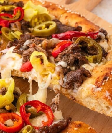 Philly steak pizza served hot with creamy cheese sauce and peppers