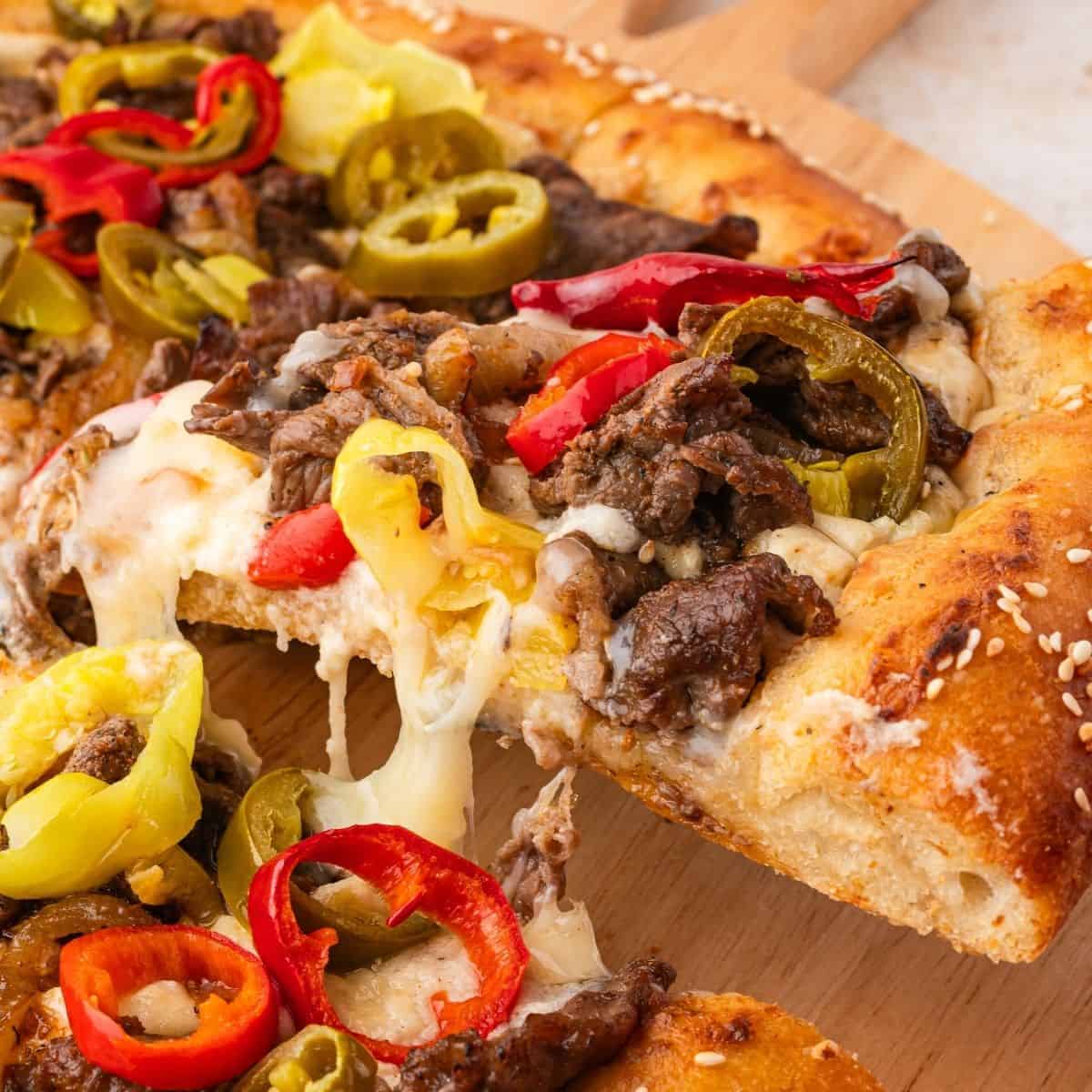 Philly steak pizza served hot with creamy cheese sauce and peppers