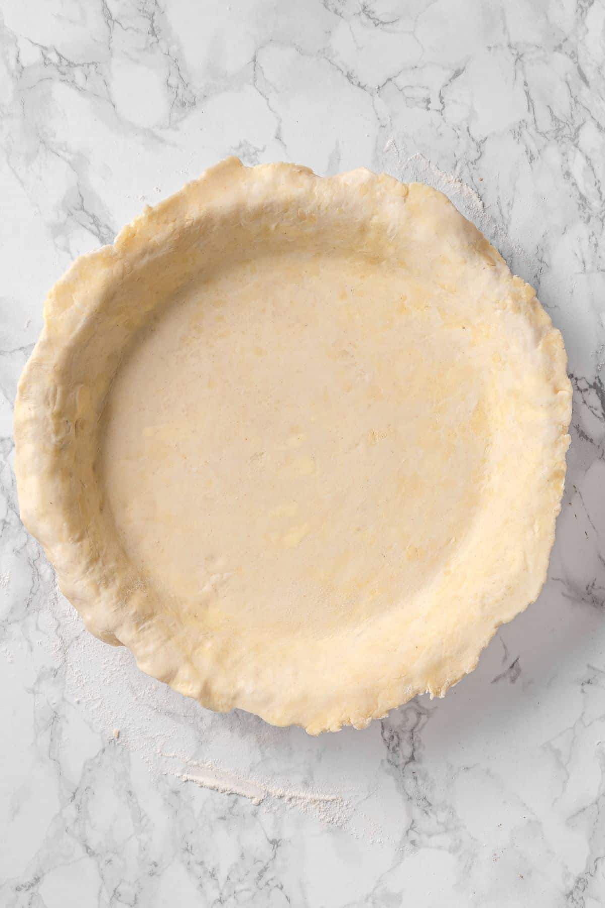 all butter pie crust recipe in a pie plate pressed and ready for trimming