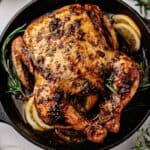 Whole chicken roasted over lemon slices in a cast iron skillet