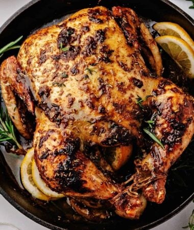 Whole chicken roasted over lemon slices in a cast iron skillet
