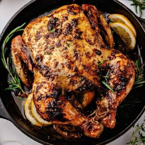 Whole chicken roasted over lemon slices in a cast iron skillet