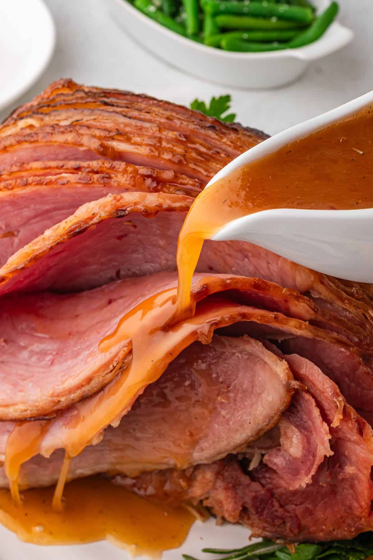 crockpot ham on a serving platter with honey brown sugar glaze being poured over the top of it