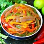 red, yellow, and green bell peppers cooked in a bowl with red onions