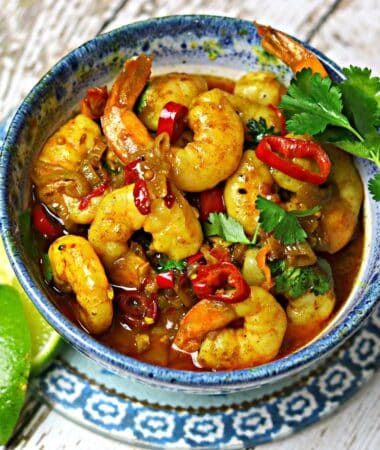 Indian shrimp curry in a blue bowl with cilantro and lime wedges