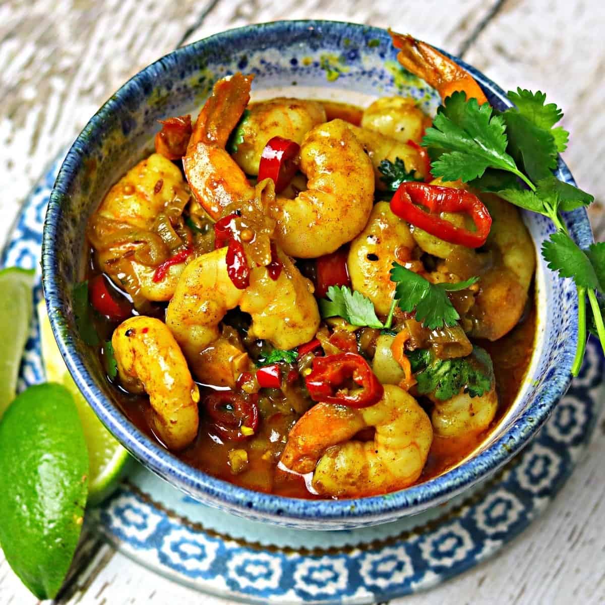 Indian shrimp curry in a blue bowl with cilantro and lime wedges