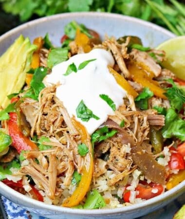 a keto burrito bowl with cauliflower rice, fajita veggies, pork carnitas, sour cream and sliced tomatoes