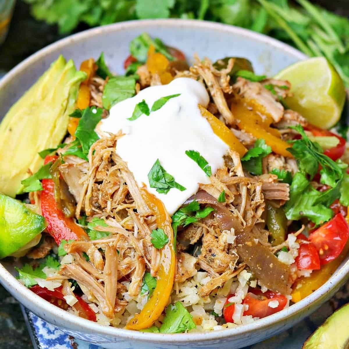 a keto burrito bowl with cauliflower rice, fajita veggies, pork carnitas, sour cream and sliced tomatoes