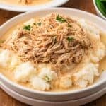 slow cooker chicken and gravy on a plate with mashed potatoes and fresh parsley ready to be served