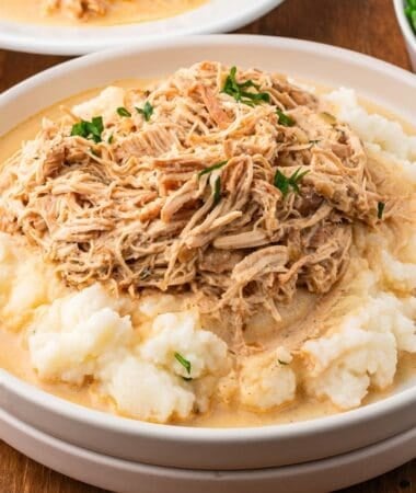 slow cooker chicken and gravy on a plate with mashed potatoes and fresh parsley ready to be served
