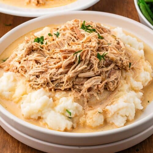 slow cooker chicken and gravy on a plate with mashed potatoes and fresh parsley ready to be served