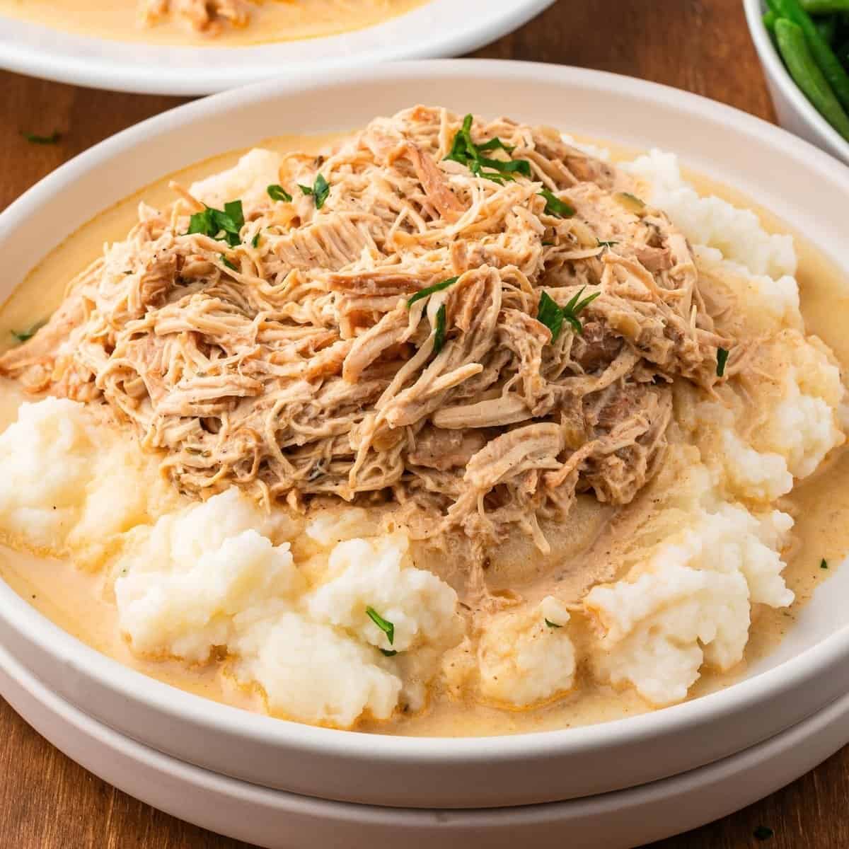 slow cooker chicken and gravy on a plate with mashed potatoes and fresh parsley ready to be served