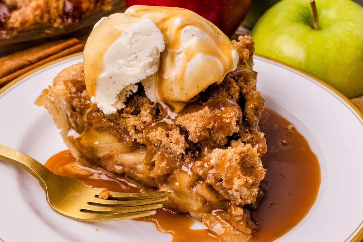a slice of dutch apple pie on a plate topped with vanilla ice cream and salted caramel sauce