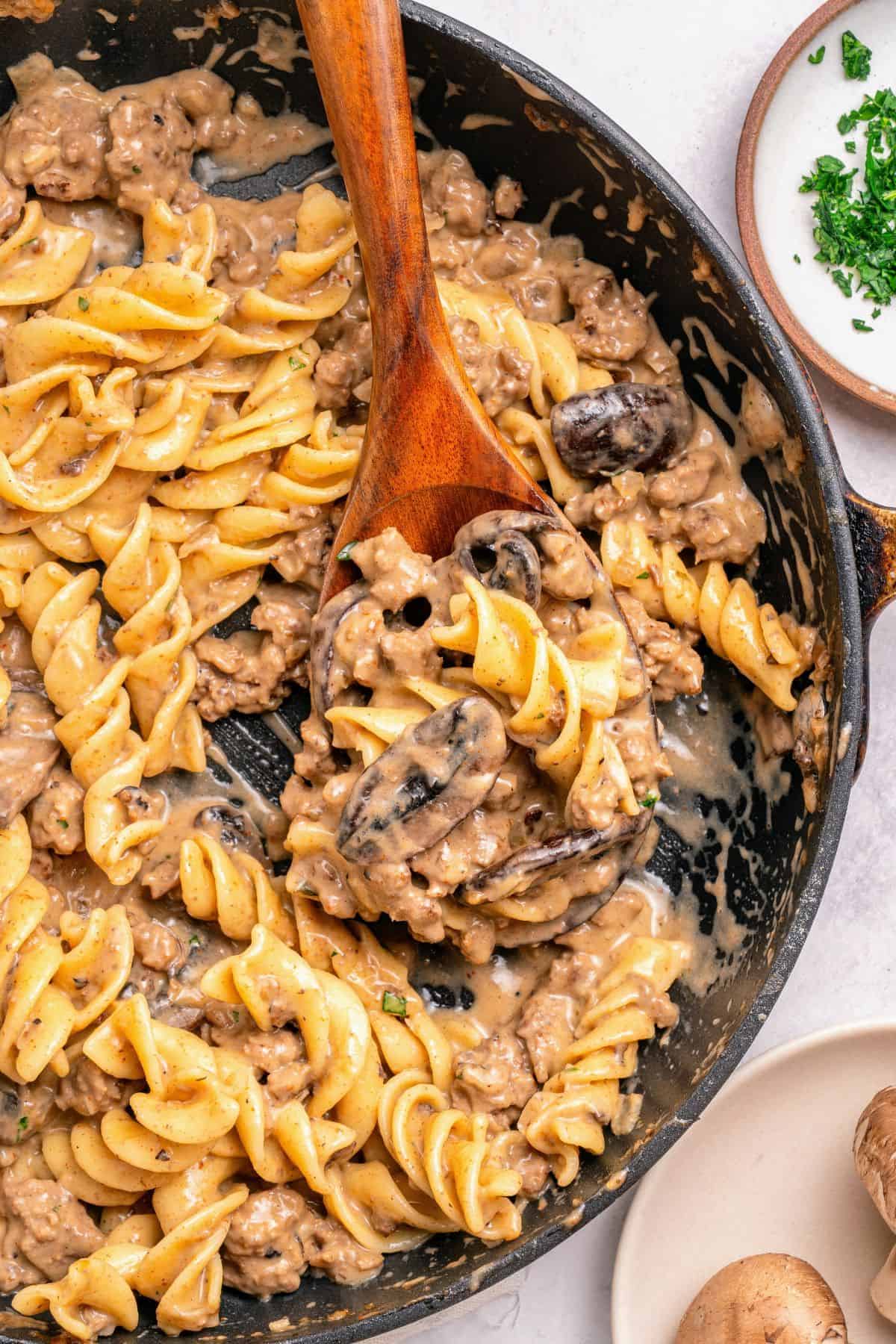 creamy ground beef stroganoff recipe in a skillet with a wooden spoon scooping some out