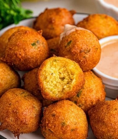 Golden Southern hush puppies served on a plate alongside a bowl of dipping sauce