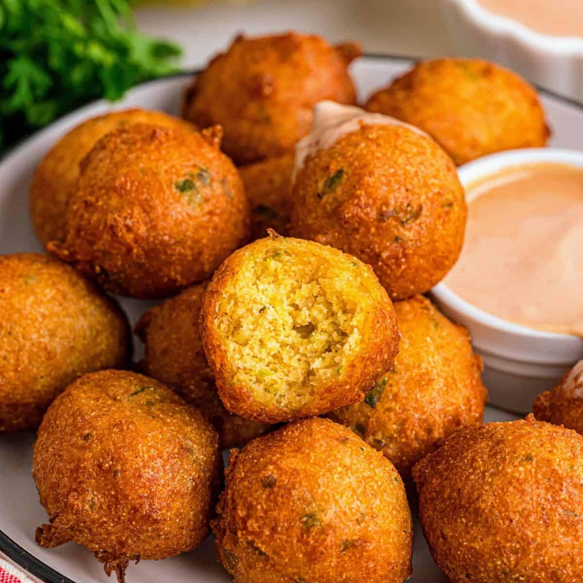 Golden Southern hush puppies served on a plate alongside a bowl of dipping sauce
